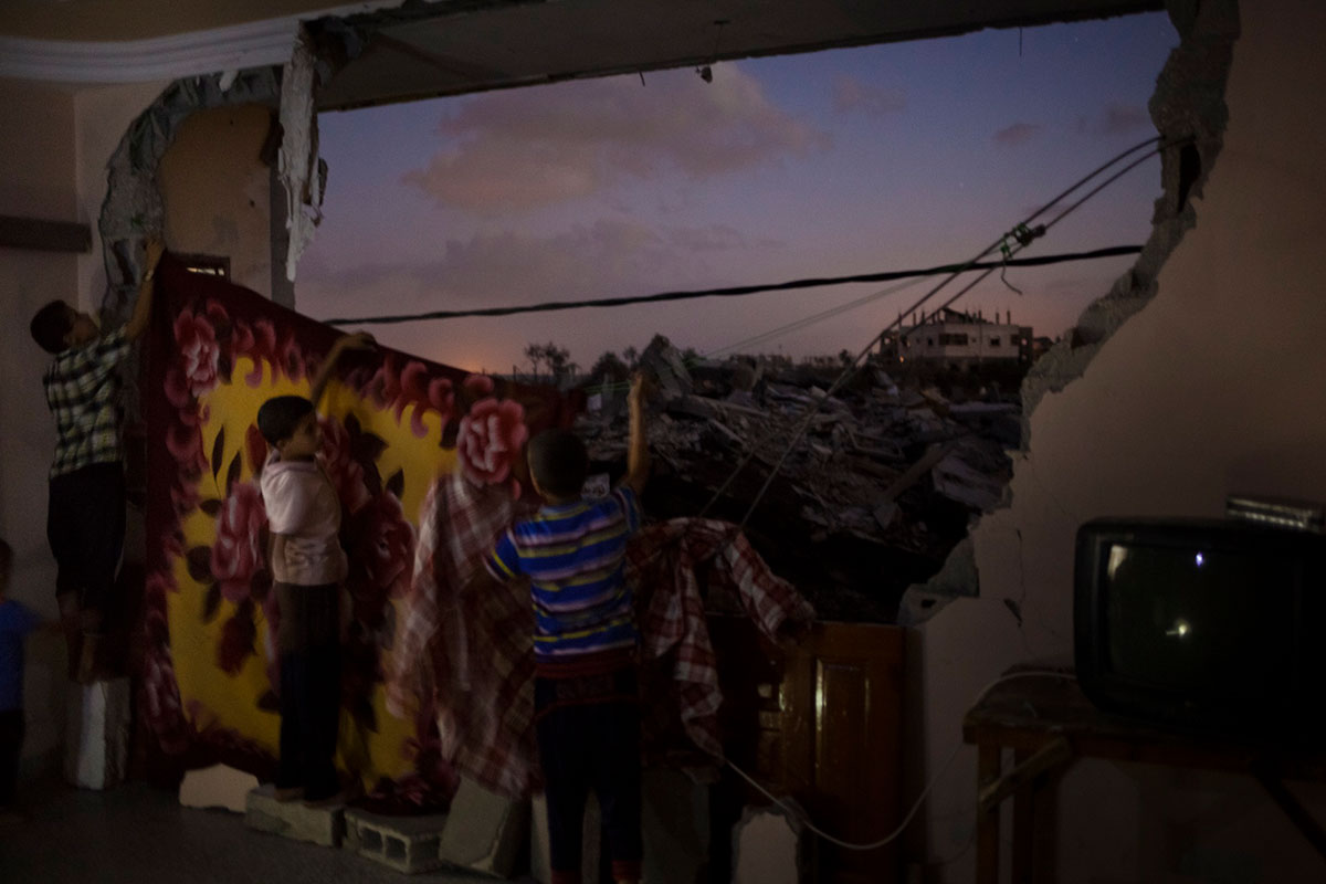 Bildetekst: Barna i Haraara-familien i Gaza henger opp tepper for å skjule ruinene utenfor soverommet dems. Familien har flyttet tilbake i leiligheten siden de ikke har noe annet sted å bo. Nabolaget deres ble svært ødelagt av krigen i sommeren 2014. Totalt ble over 100.000 hjem ødelagt eller skadet.